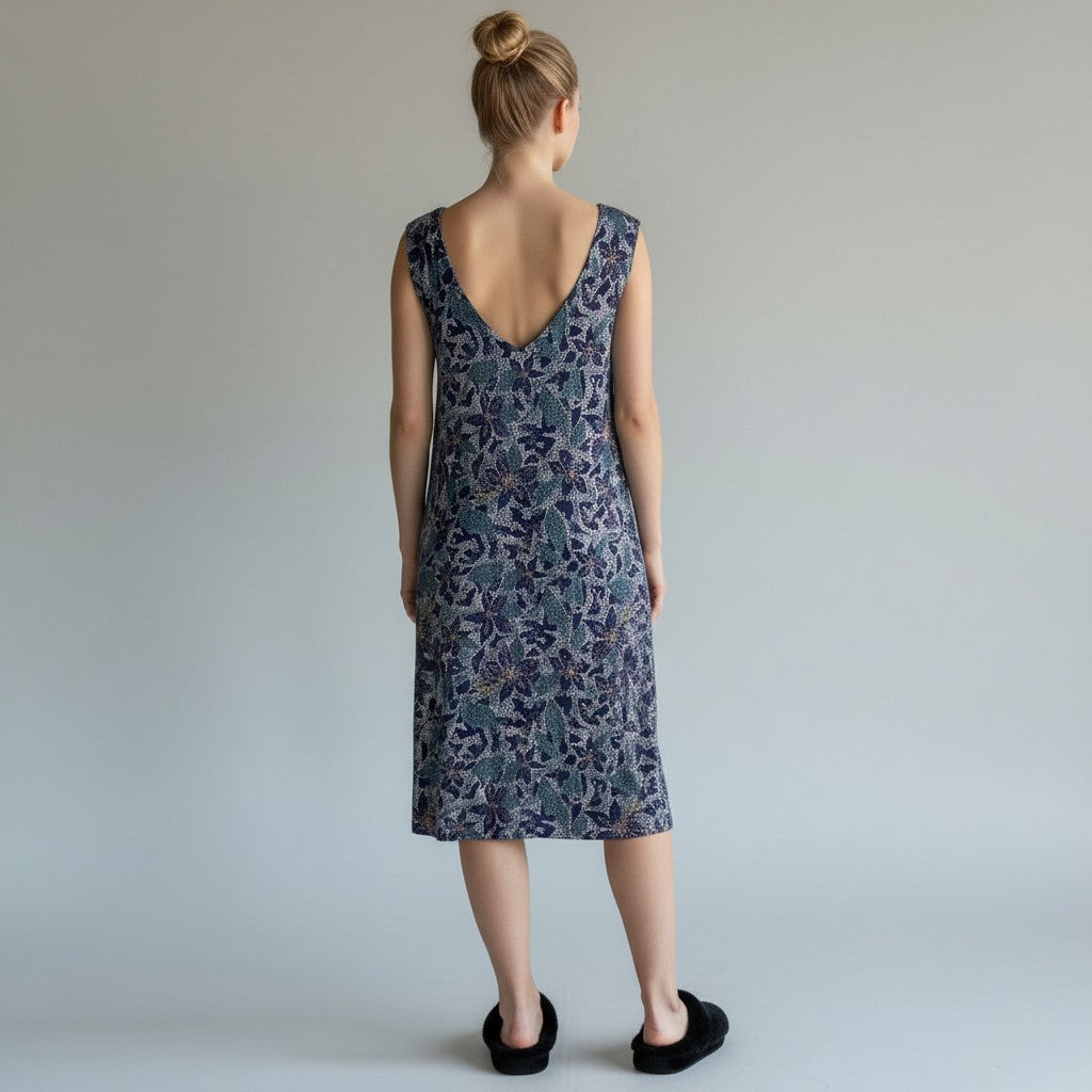 A woman wearing a floral print dress with no sleeves and black fuzzy slippers on alight gray studio background.
