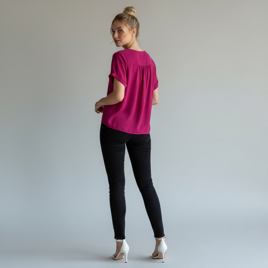 A woman wearing a bright magenta short-sleeve top, black skinny jeans, and white high heels, photographed from the back against a light gray studio background.