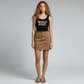A model stands against a light gray studio background wearing a black tank top with white text reading 'Reclaimed Revival Boutique' and a brown mini skirt.