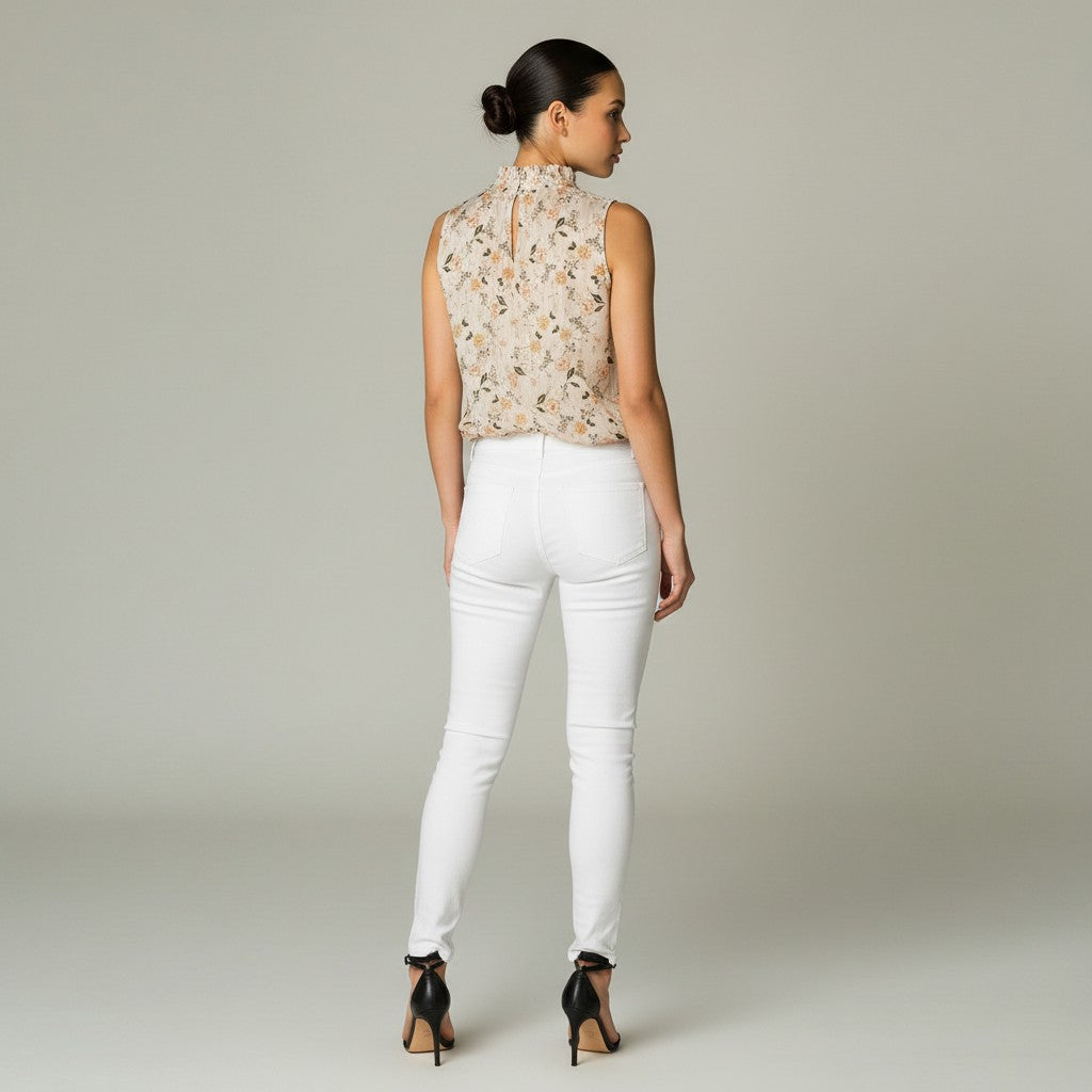 A woman is shown from the back wearing a sleeveless beige floral blouse and white skinny jeans with black high heels, set against a neutral light gray studio background.