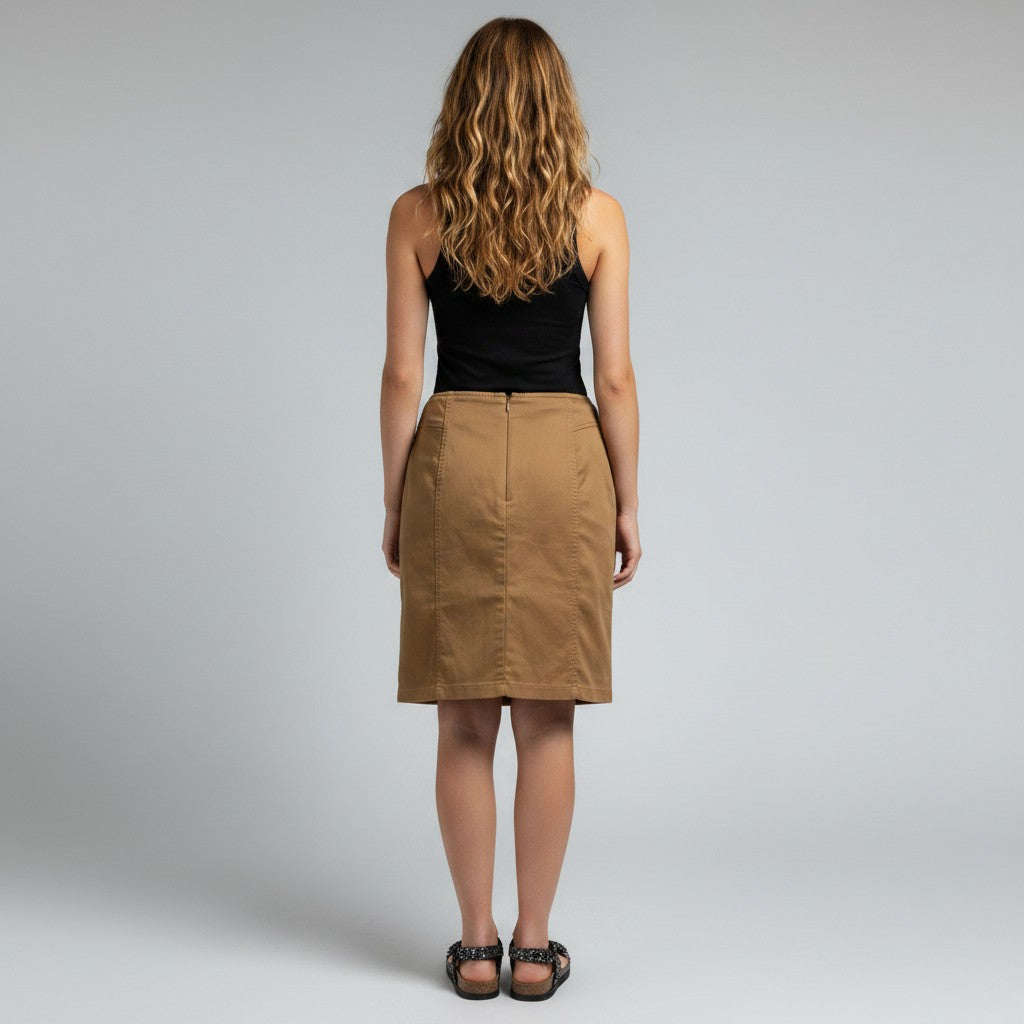 A woman viewed from behind wearing a black sleeveless top and a knee-length tan skirt, standing against a light gray studio background.