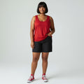 A woman modeling a sleeveless red scoop-neck tank top, black denim shorts, and red low-top sneakers against a light gray studio background.