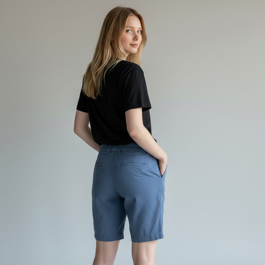 A woman wearing a black short-sleeve t-shirt and blue shorts, photographed from the back against a plain light gray studio background.
