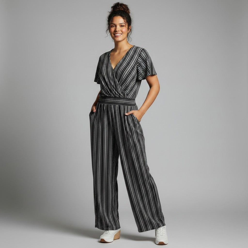 A woman modeling a black and white vertically striped short-sleeve wrap jumpsuit with wide legs, standing against a neutral gray studio background.
