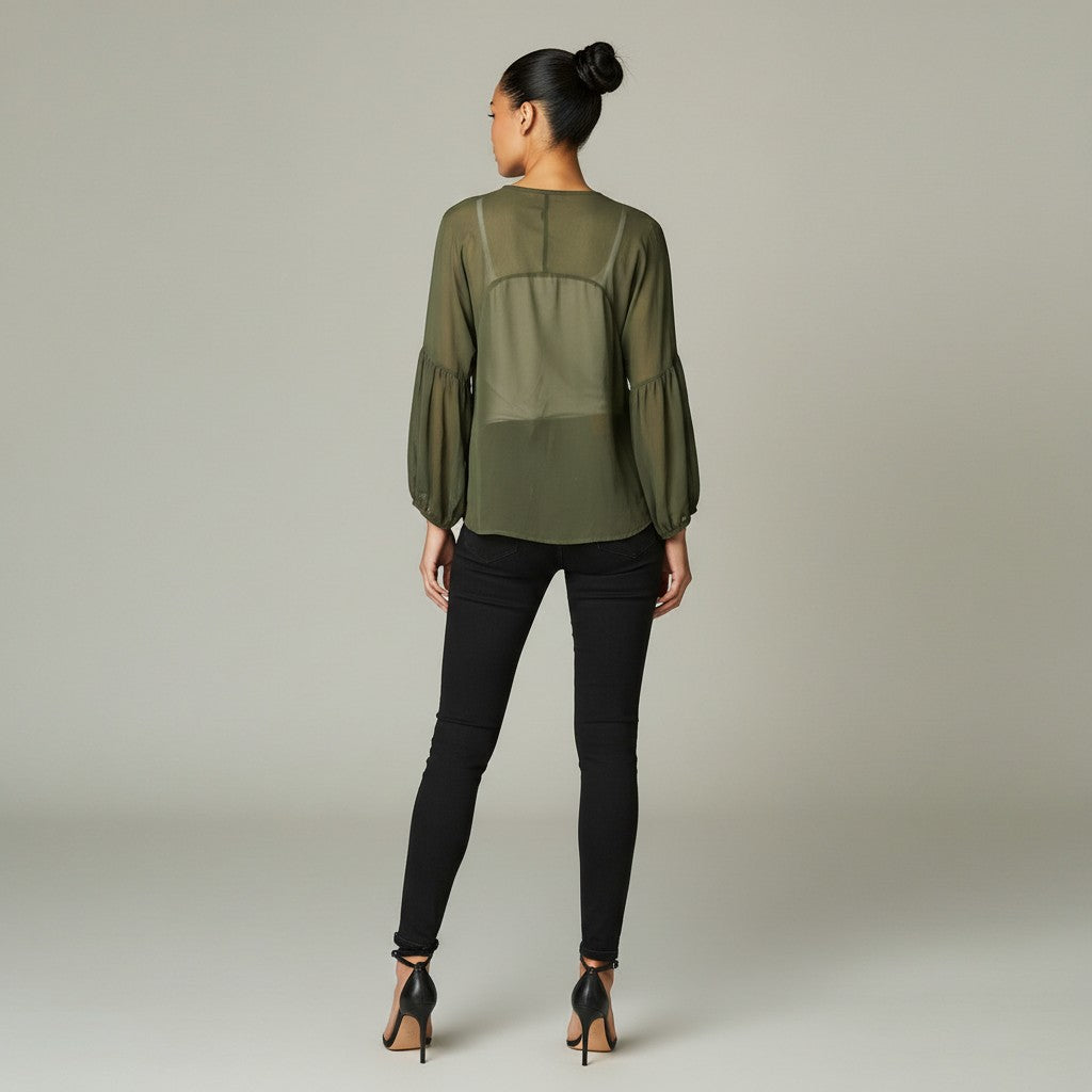 A woman viewed from the back wearing an olive green sheer long-sleeve blouse with gathered sleeves and black skinny pants, standing against a light gray studio background.