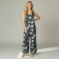 A woman modeling a sleeveless wide-leg jumpsuit with a black base and white floral pattern, standing against a neutral light gray studio background.