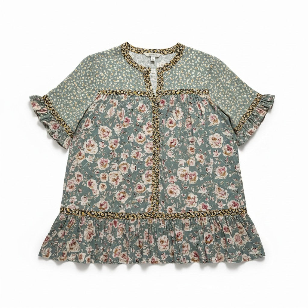a short-sleeved, tiered bohemian-style dress with a green and beige floral pattern against a neutral gray studio background.