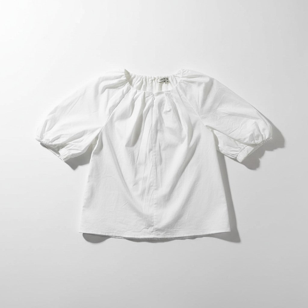A white short-sleeve blouse with a gathered, ruffled neckline and puff sleeves, laid flat on a light gray background.