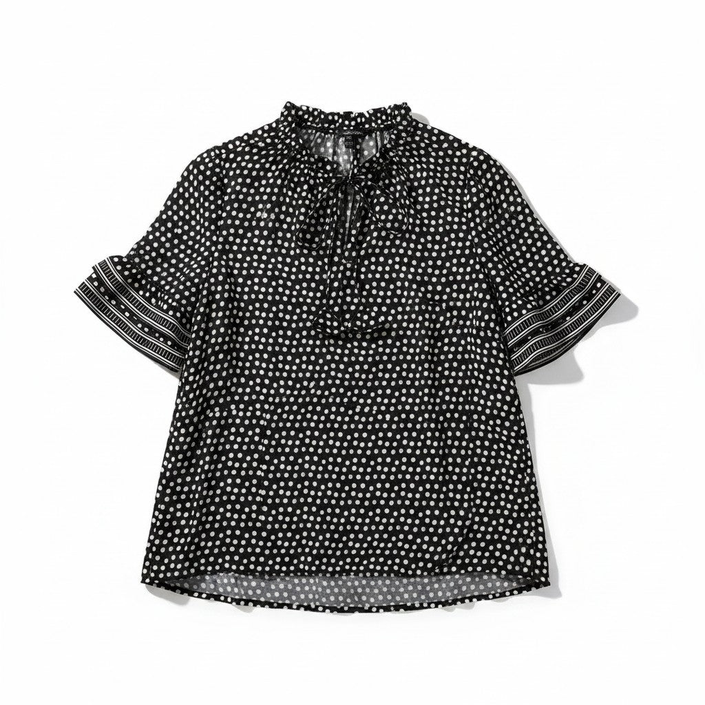 A black short-sleeve blouse with a white polka dot pattern, featuring a ruffled tie-neck collar and striped ruffled sleeves, laid flat on a white background.