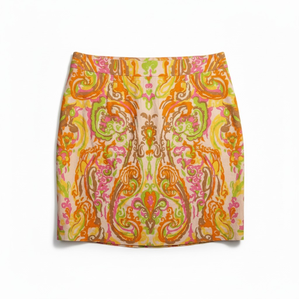 A women's mini skirt featuring a vibrant, symmetrical paisley and ornamental pattern in orange, pink, green, and yellow on a light beige base, shown flat against a white background.