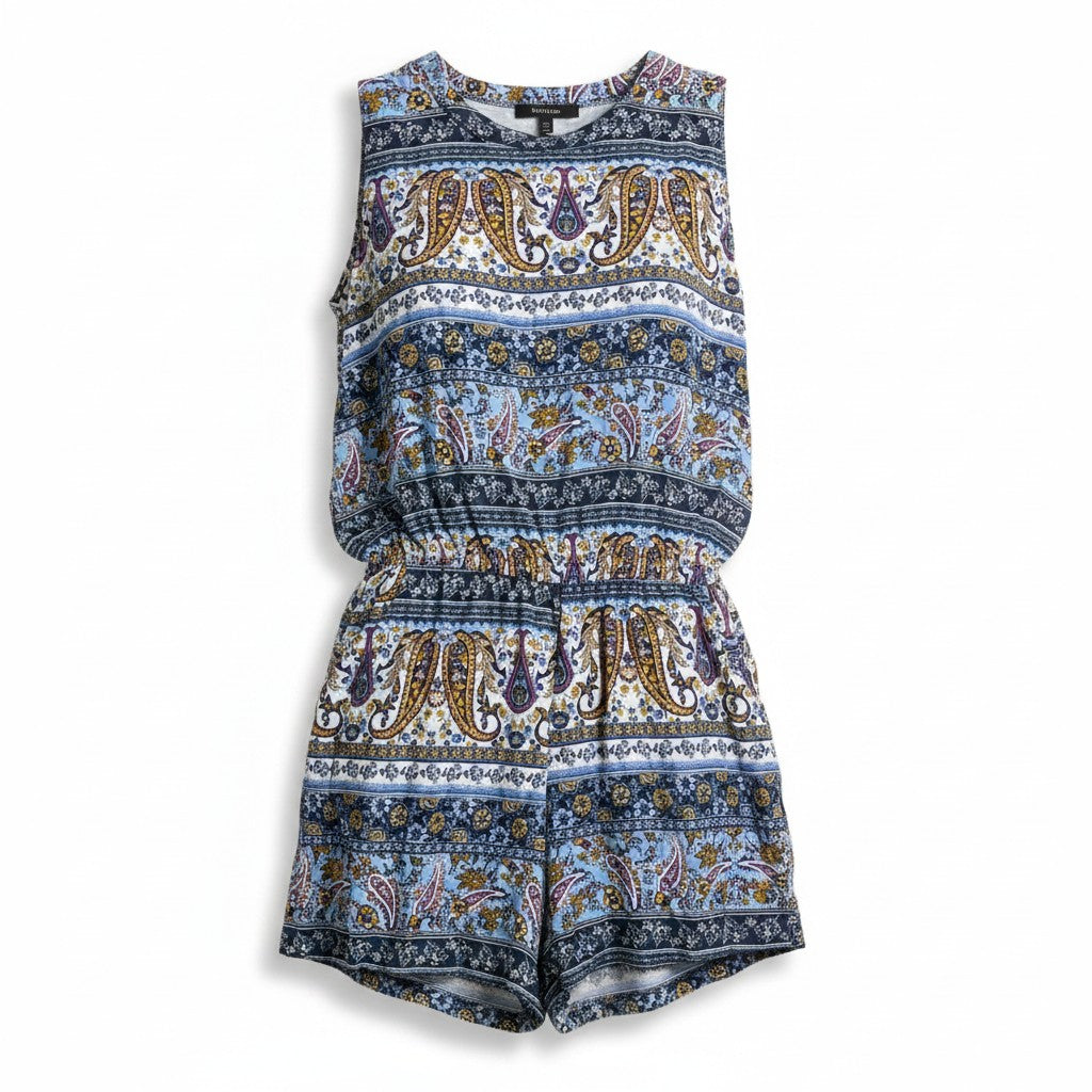 A sleeveless jumpsuit with an intricate paisley and floral pattern in shades of blue, navy, gold, and white, displayed against a clean white background.