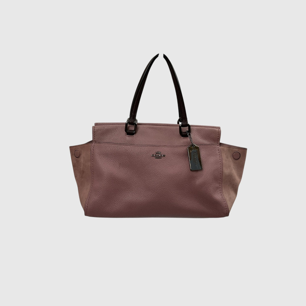 A dusty rose pebbled leather tote bag with black leather handles and a small metal logo plaque on the front, shown against a light gray background.