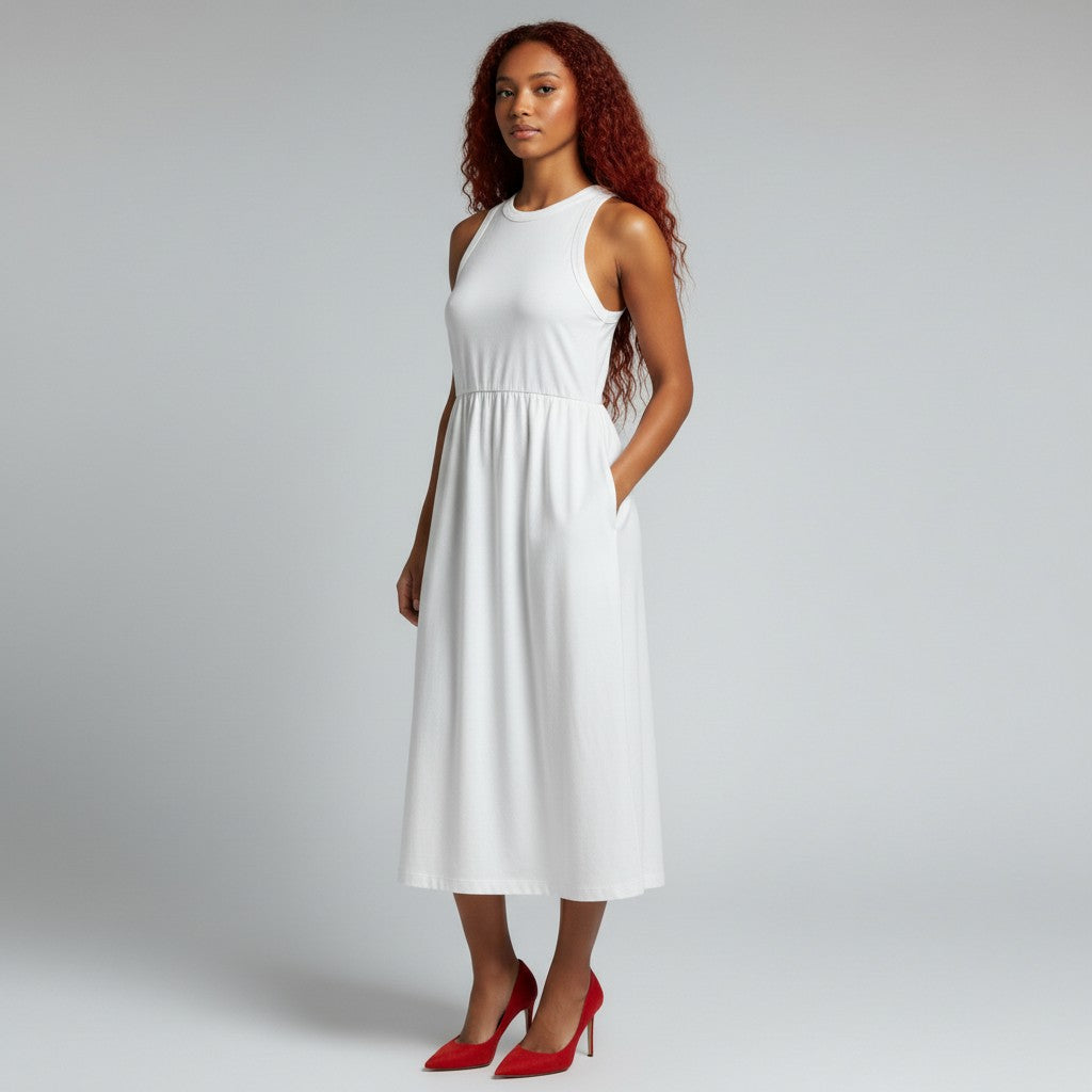 A woman modeling a sleeveless white midi dress with side pockets, paired with red high heels, against a light gray studio background.