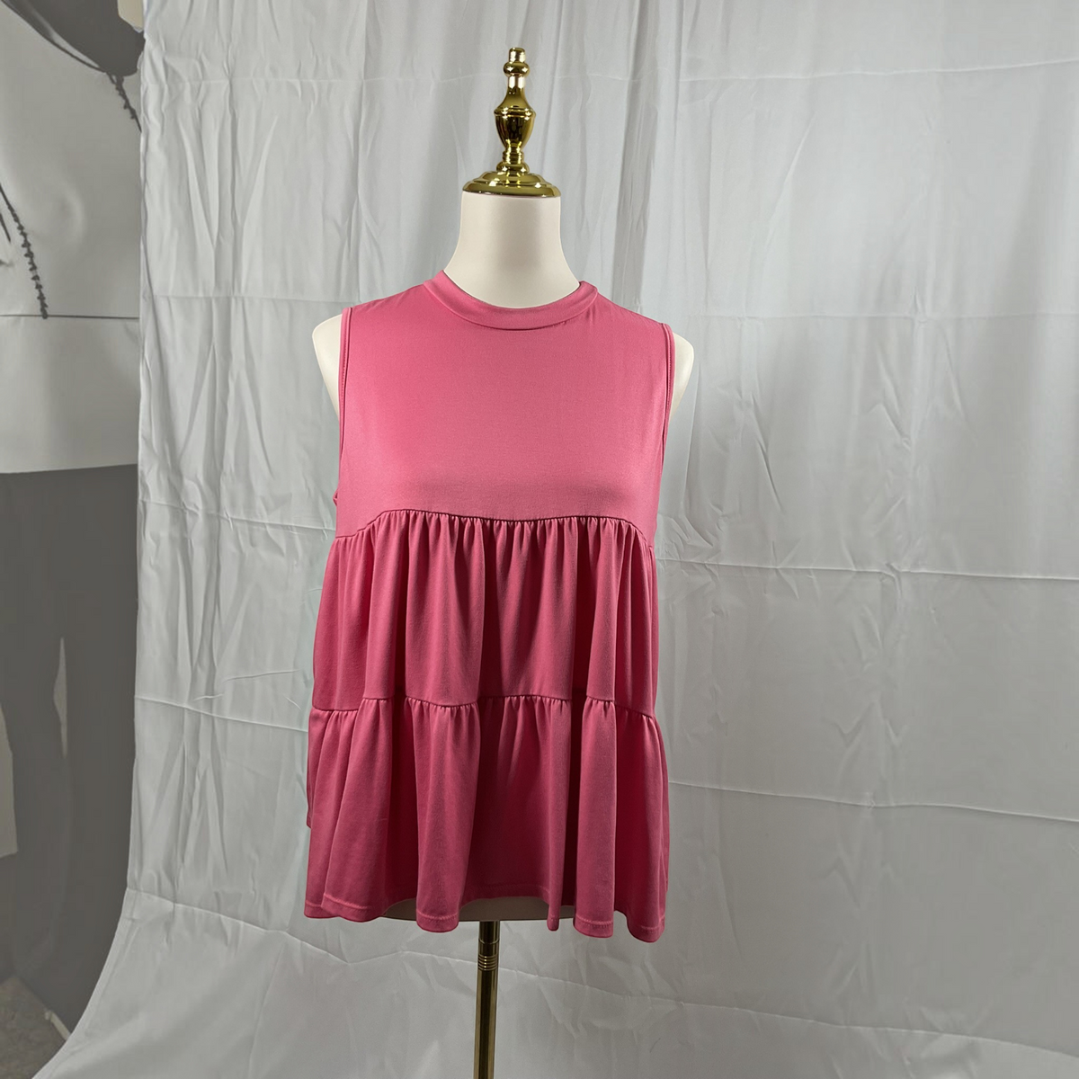 a woman wearing a pink shirt with white jeans on a light gray studio background.