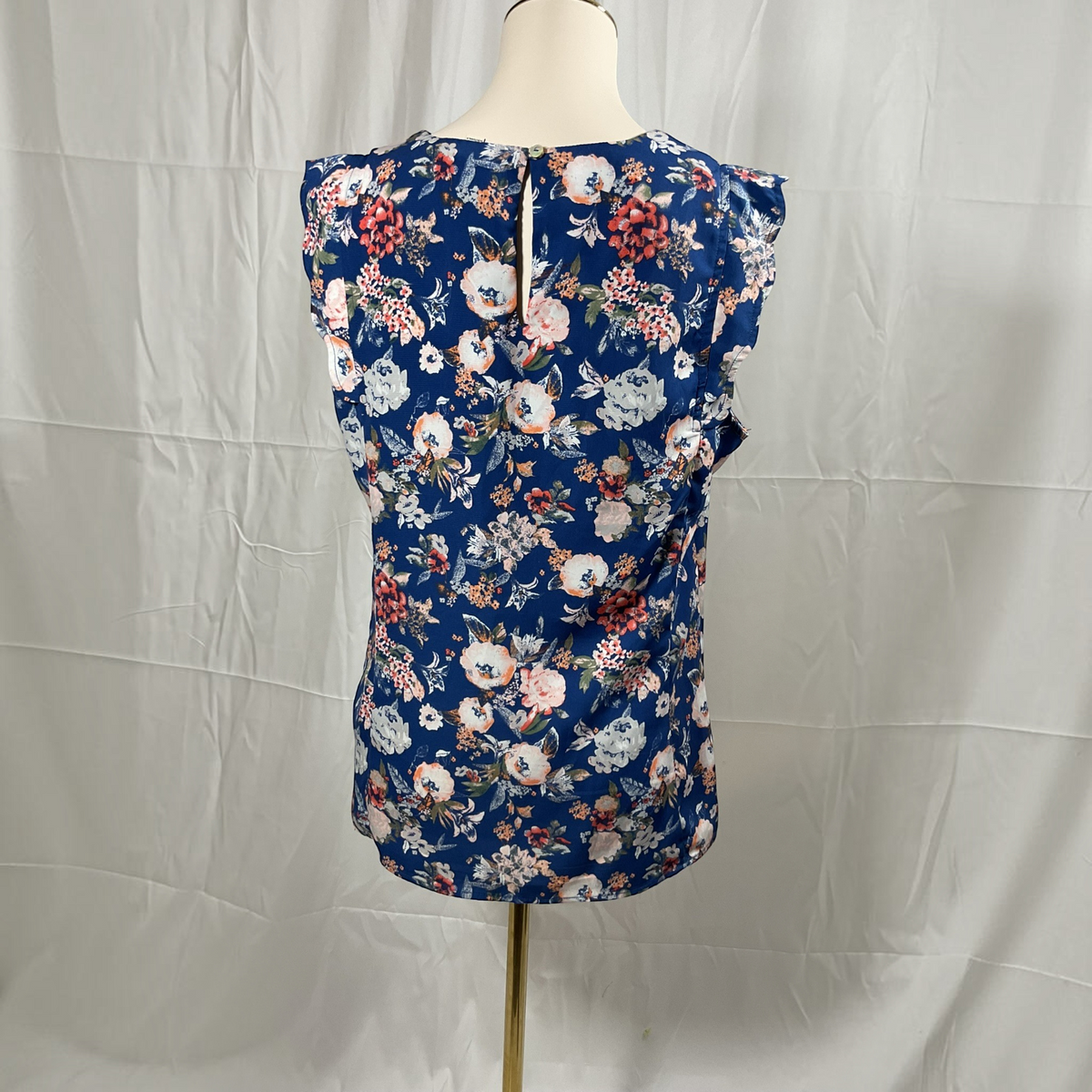 A sleeveless navy blue blouse with a dense floral print in pink, white, and red, displayed on a cream mannequin torso against a wrinkled white fabric backdrop.