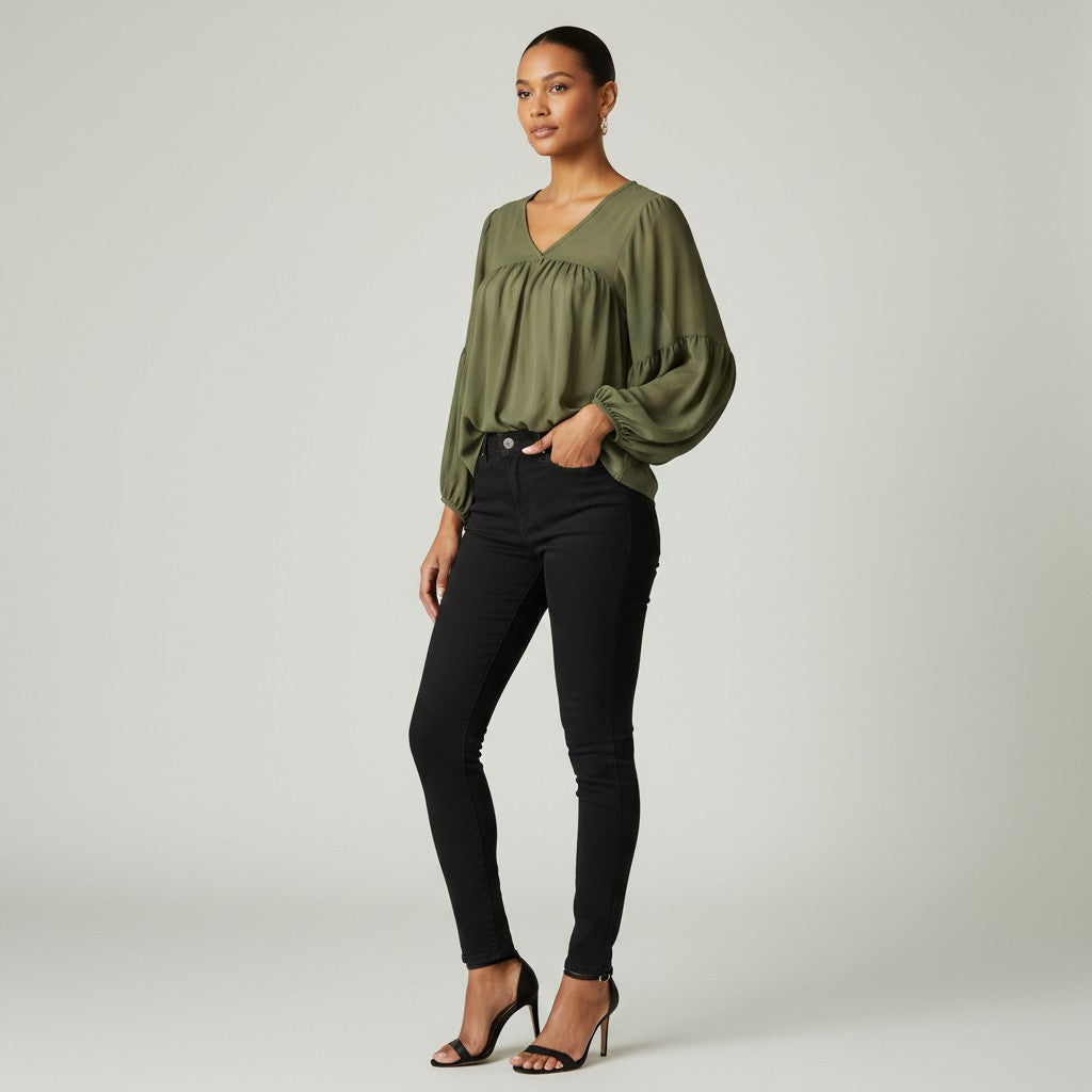 A woman modeling a loose, olive green long-sleeve blouse with a gathered neckline, paired with black skinny jeans and black high-heeled sandals, against a light gray studio background.