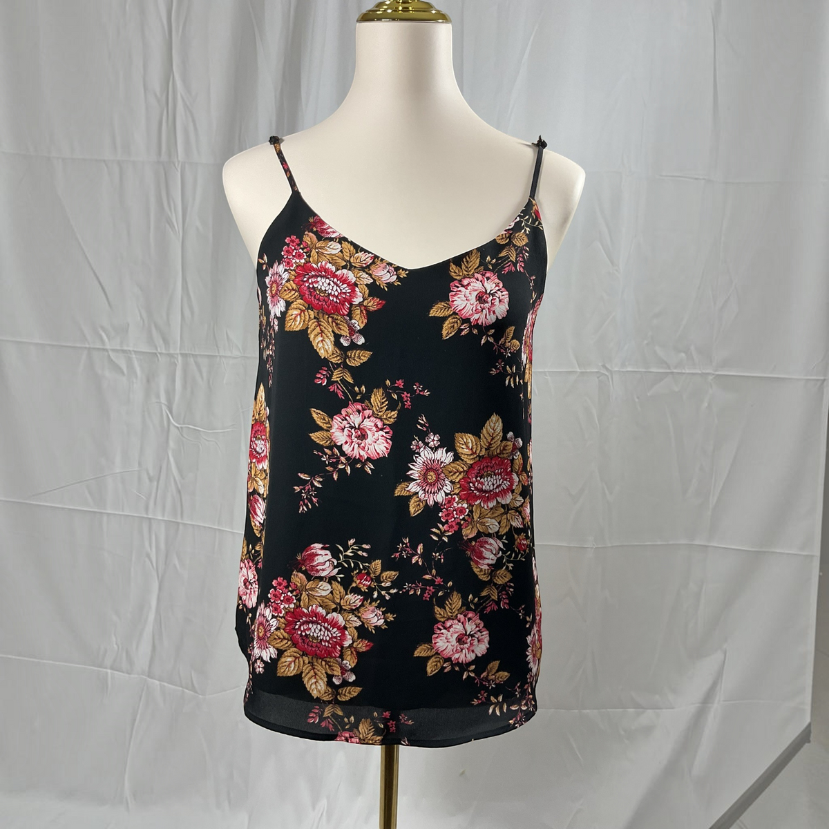 A black spaghetti-strap camisole top with a red, pink, and gold floral pattern, displayed on a cream mannequin torso against a wrinkled white backdrop.