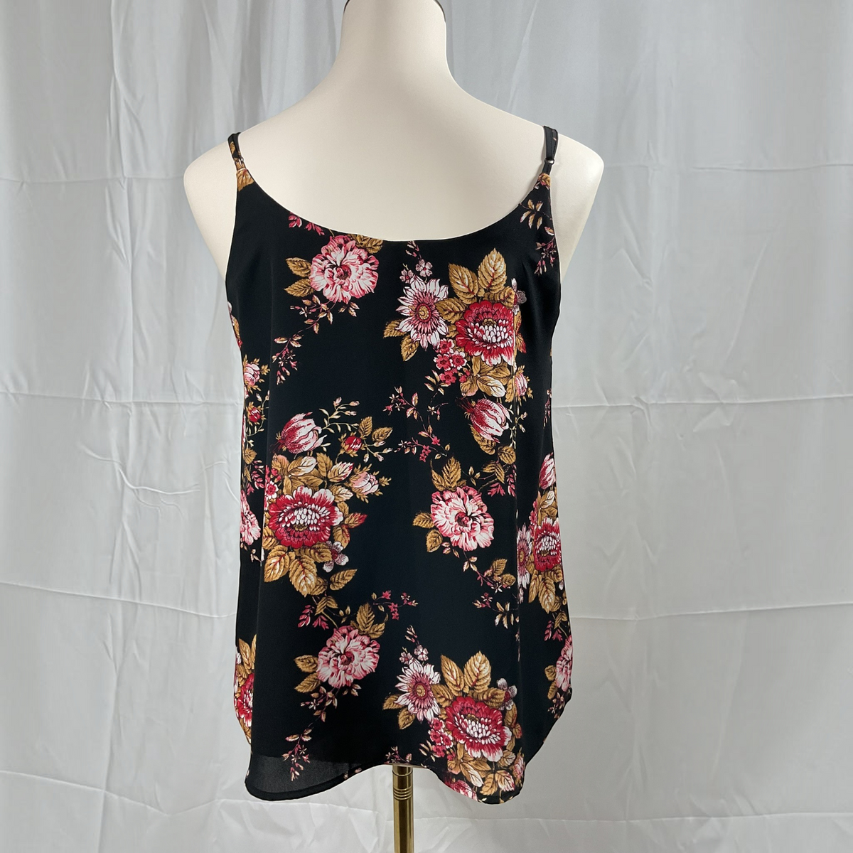 A black spaghetti-strap camisole top with a red, pink, and gold floral pattern, displayed on a cream mannequin torso against a wrinkled white backdrop.