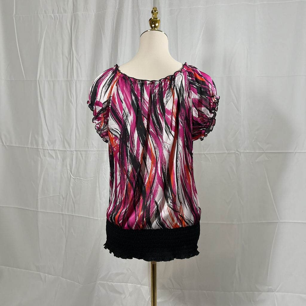A short-sleeve blouse with puff sleeves and an abstract brushstroke print in pink, black, and orange on a white base, displayed on a dress form against a white fabric backdrop.