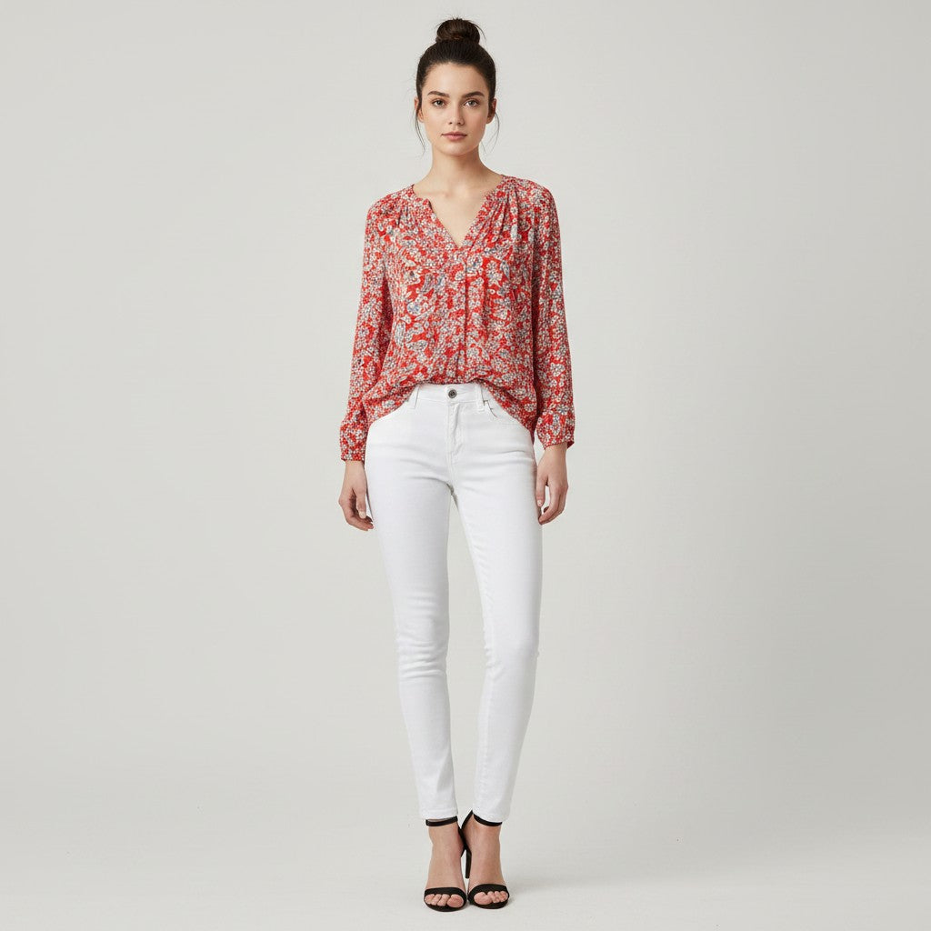 A woman modeling a red and white floral print long-sleeve blouse with white skinny jeans and black strappy heels, standing against a light gray studio background.