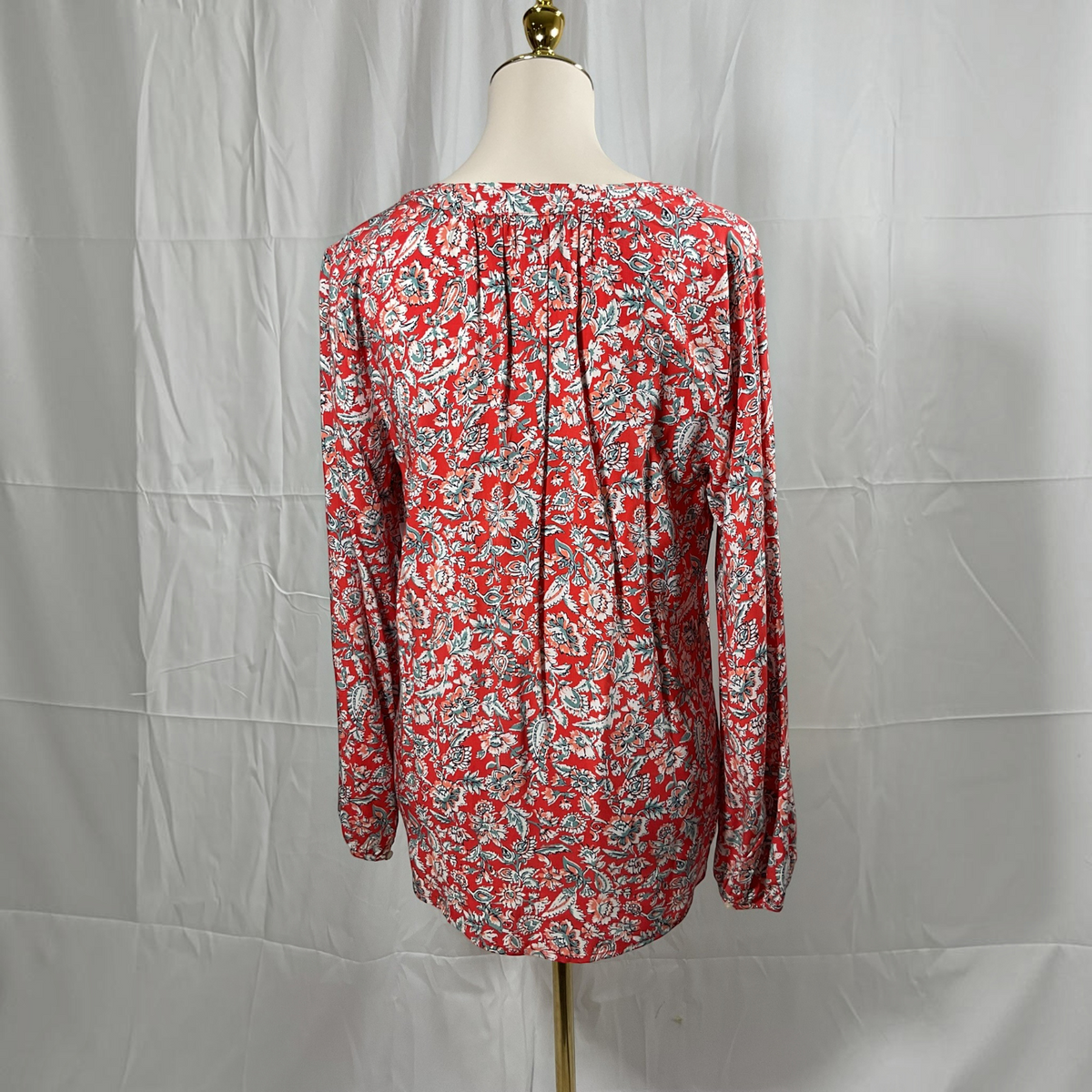 A long-sleeve blouse with a red, white, and gray floral paisley pattern, displayed on a cream dress form mannequin against a wrinkled white backdrop.