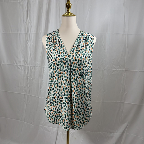 A sleeveless V-neck blouse with a green, black, and orange polka dot pattern, displayed on a white mannequin torso against a wrinkled white fabric backdrop.