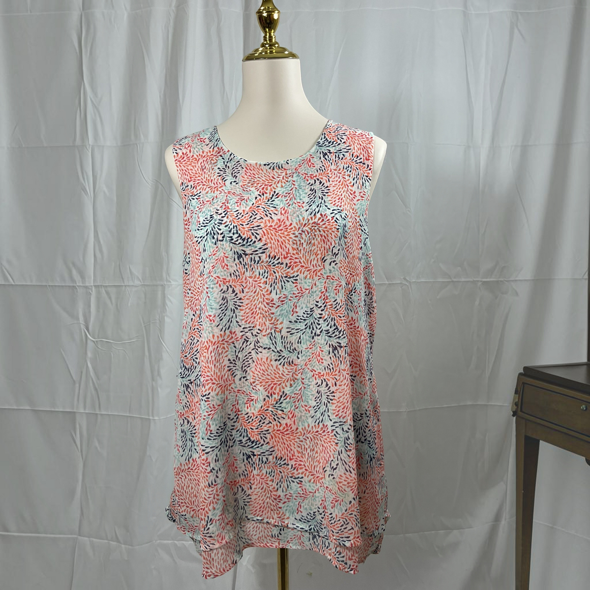 A sleeveless tunic top with a coral pink, navy, and light blue abstract floral pattern, displayed on a mannequin torso against a wrinkled white backdrop.