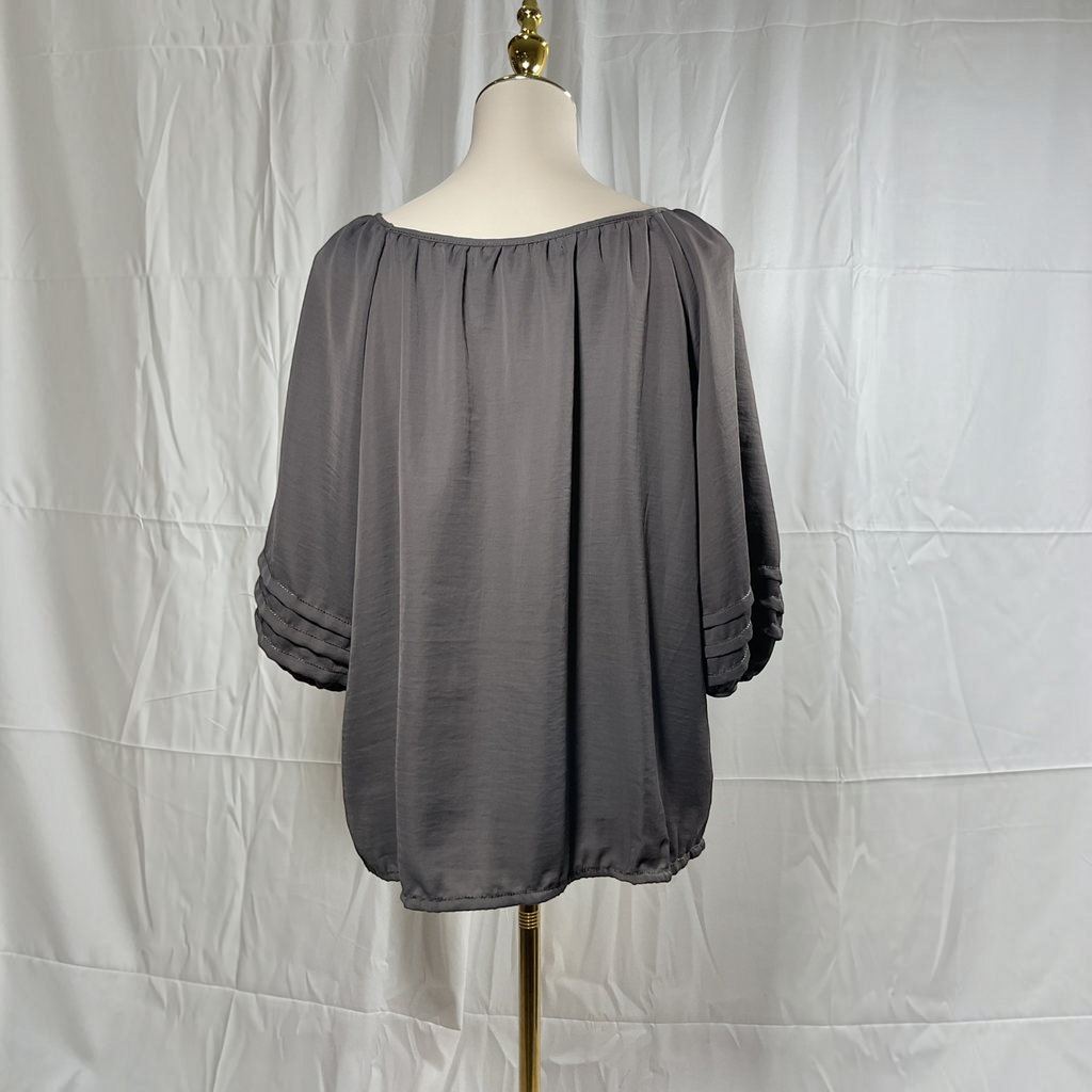 A dark gray off-the-shoulder blouse with three-quarter sleeves and gathered cuffs, displayed on a mannequin torso against a white fabric backdrop.