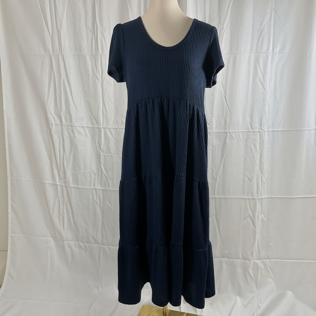 A dark navy blue ribbed knit dress with short sleeves and a tiered skirt, displayed on a mannequin against a wrinkled white backdrop.