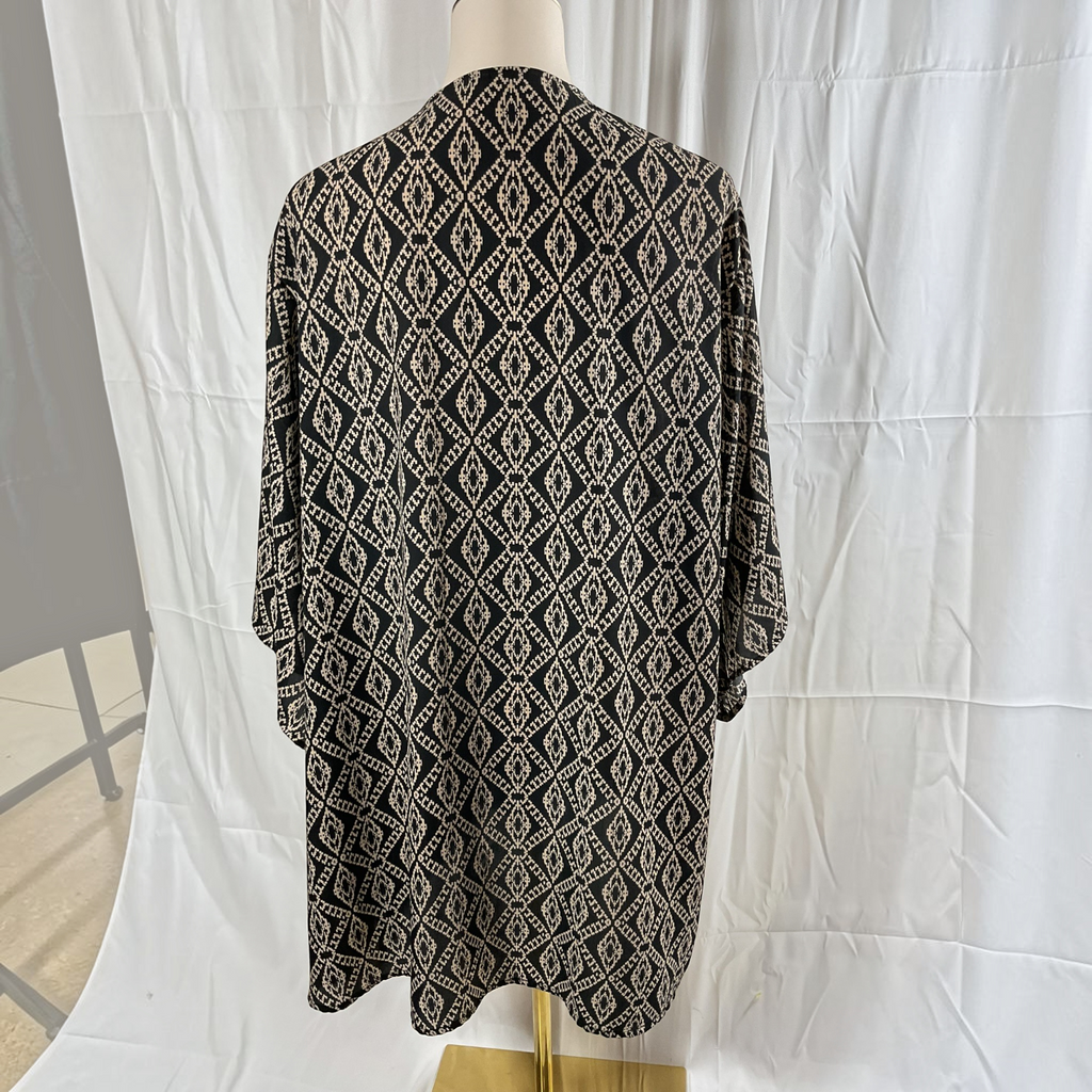 A black and beige geometric patterned tunic top displayed on a mannequin torso against a white fabric backdrop.