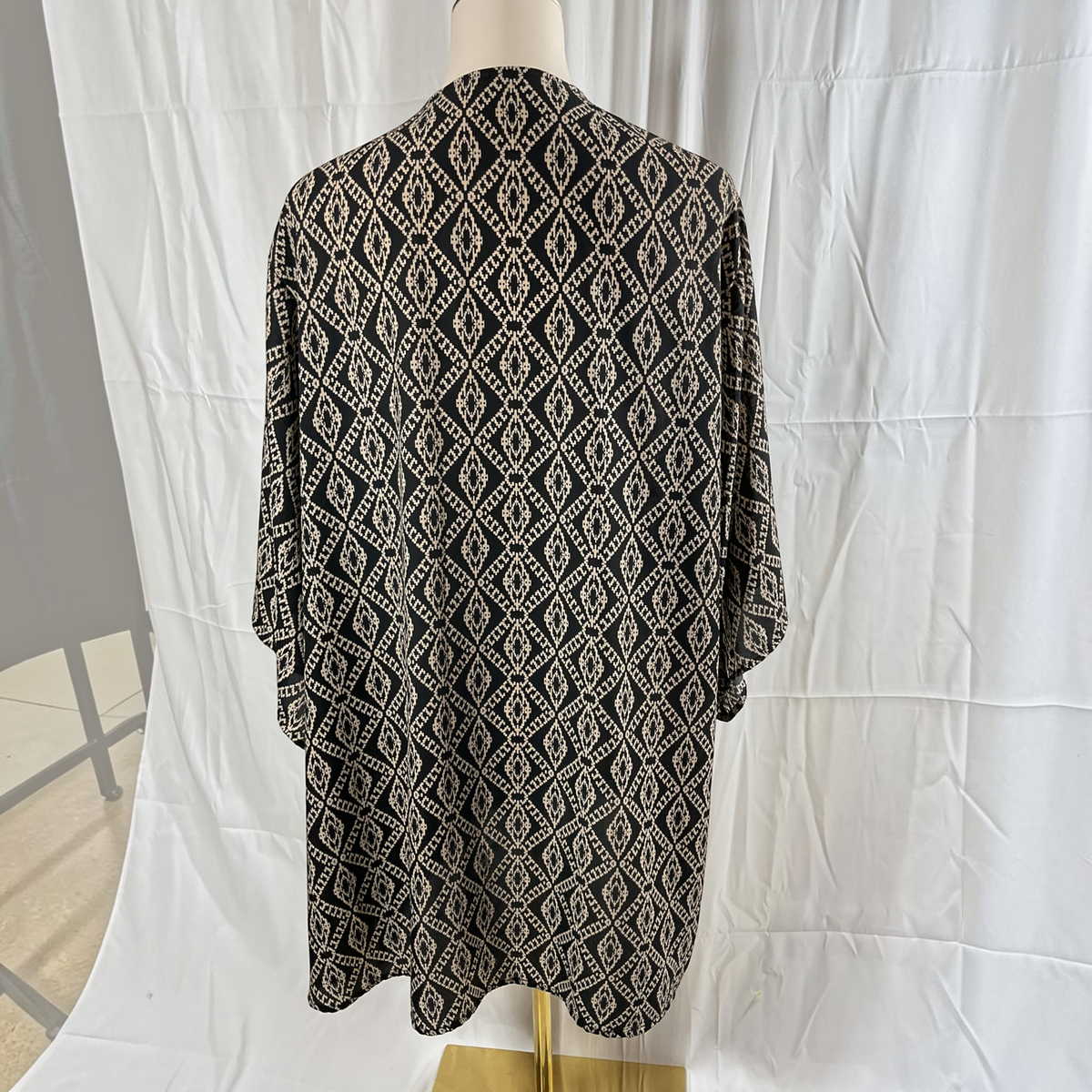 A black and beige geometric patterned tunic top displayed on a mannequin torso against a white fabric backdrop.