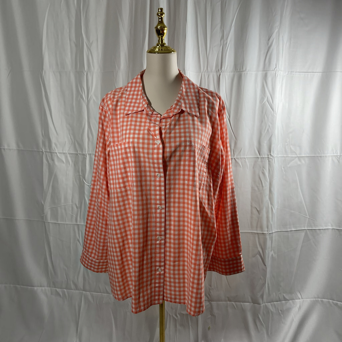 A long-sleeve button-up shirt with a red and white gingham check pattern, displayed on a white mannequin torso against a wrinkled white fabric backdrop.