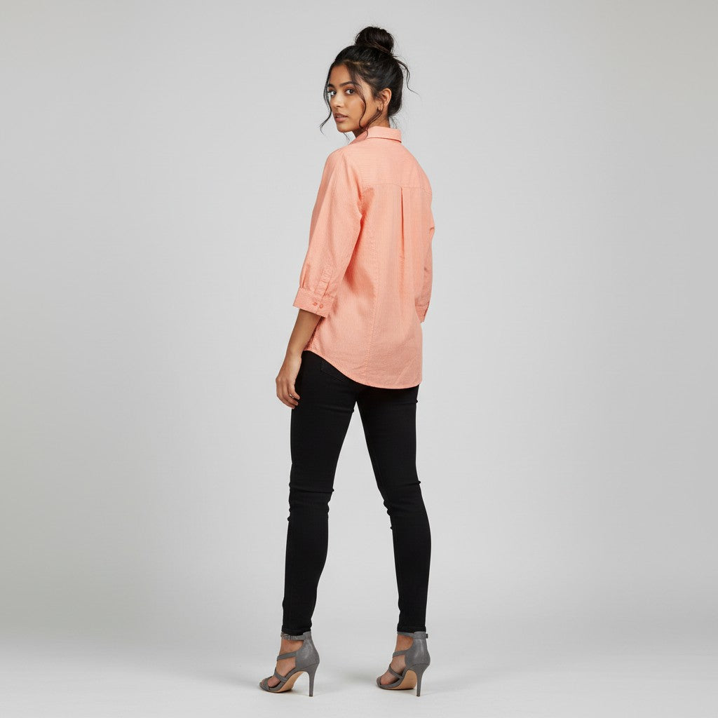 A woman modeling a peach-colored long-sleeve button-up shirt with black skinny jeans and gray strappy heels, photographed from the back against a light gray studio background.