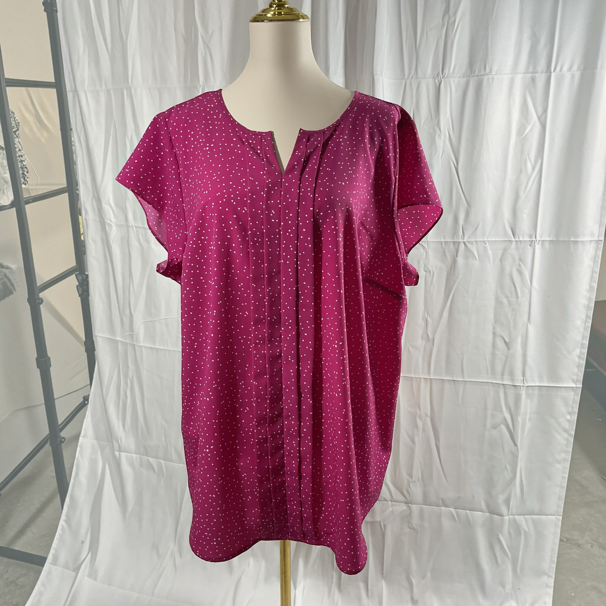 A short-sleeve magenta top with a small white polka dot pattern, displayed on a mannequin torso against a white fabric backdrop.