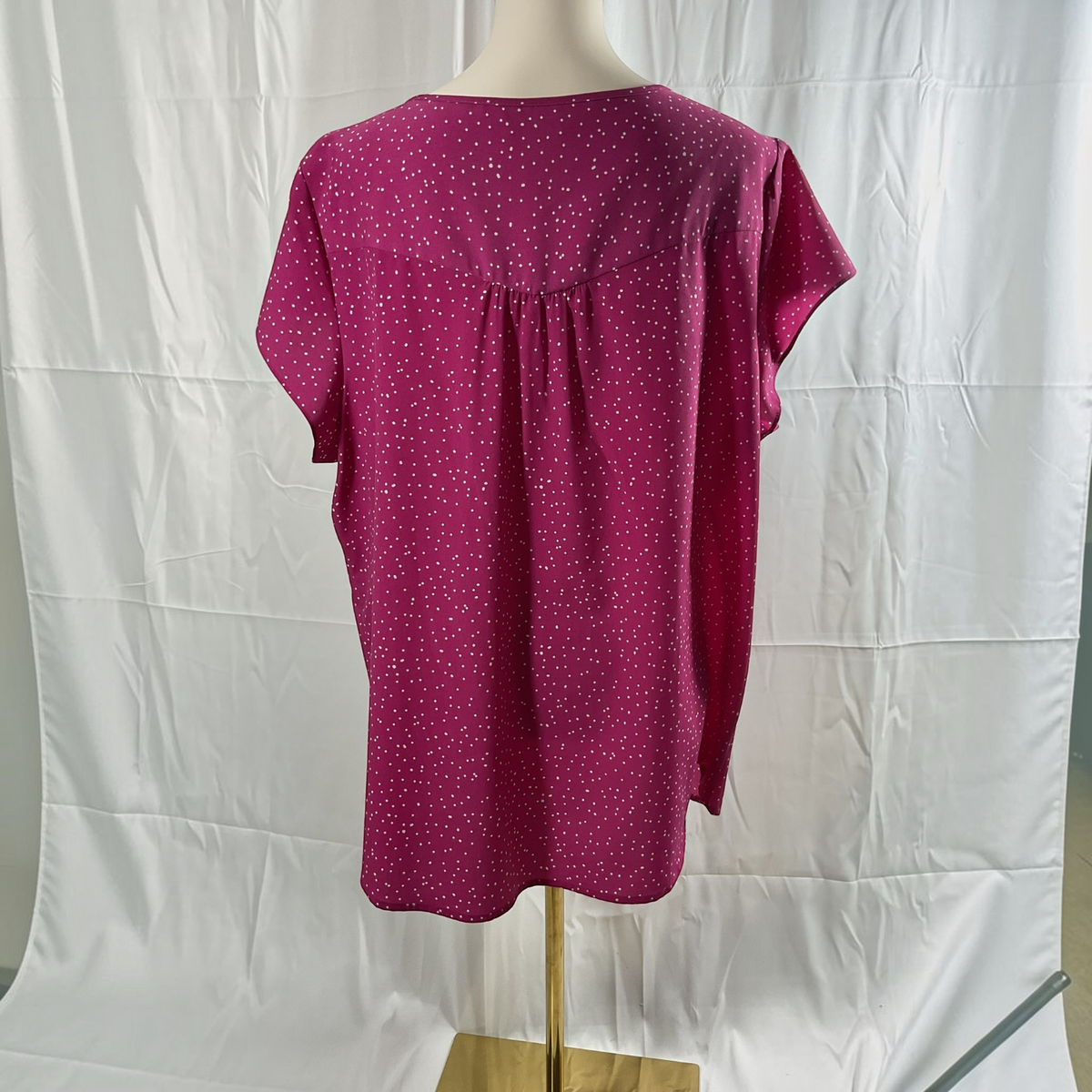 A short-sleeve top displayed on a mannequin torso against a white fabric backdrop. The top is a deep magenta pink with a small white polka dot pattern and a gathered back neckline.