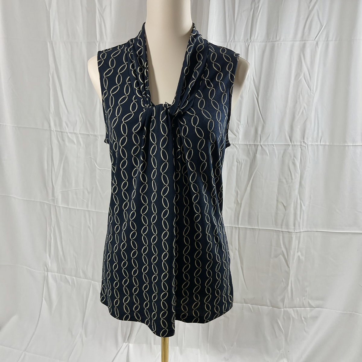 A sleeveless navy blue blouse with a cream repeating wavy line pattern, displayed on a mannequin torso against a wrinkled white fabric backdrop.