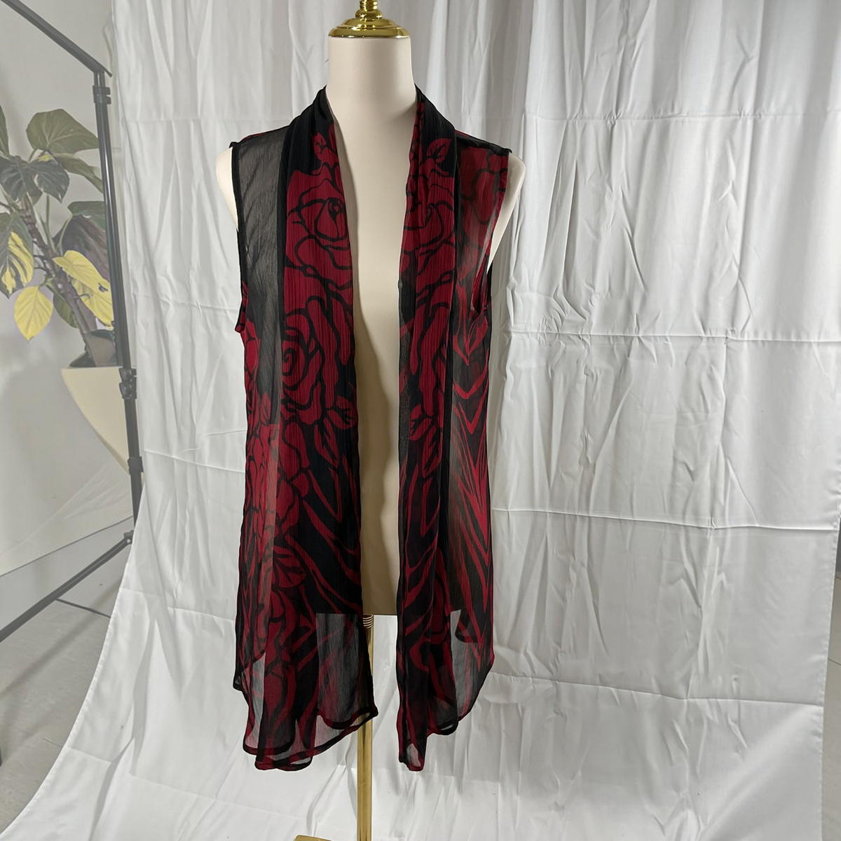 A sleeveless black mesh vest with a red rose pattern, displayed on a cream mannequin torso against a wrinkled white studio backdrop.