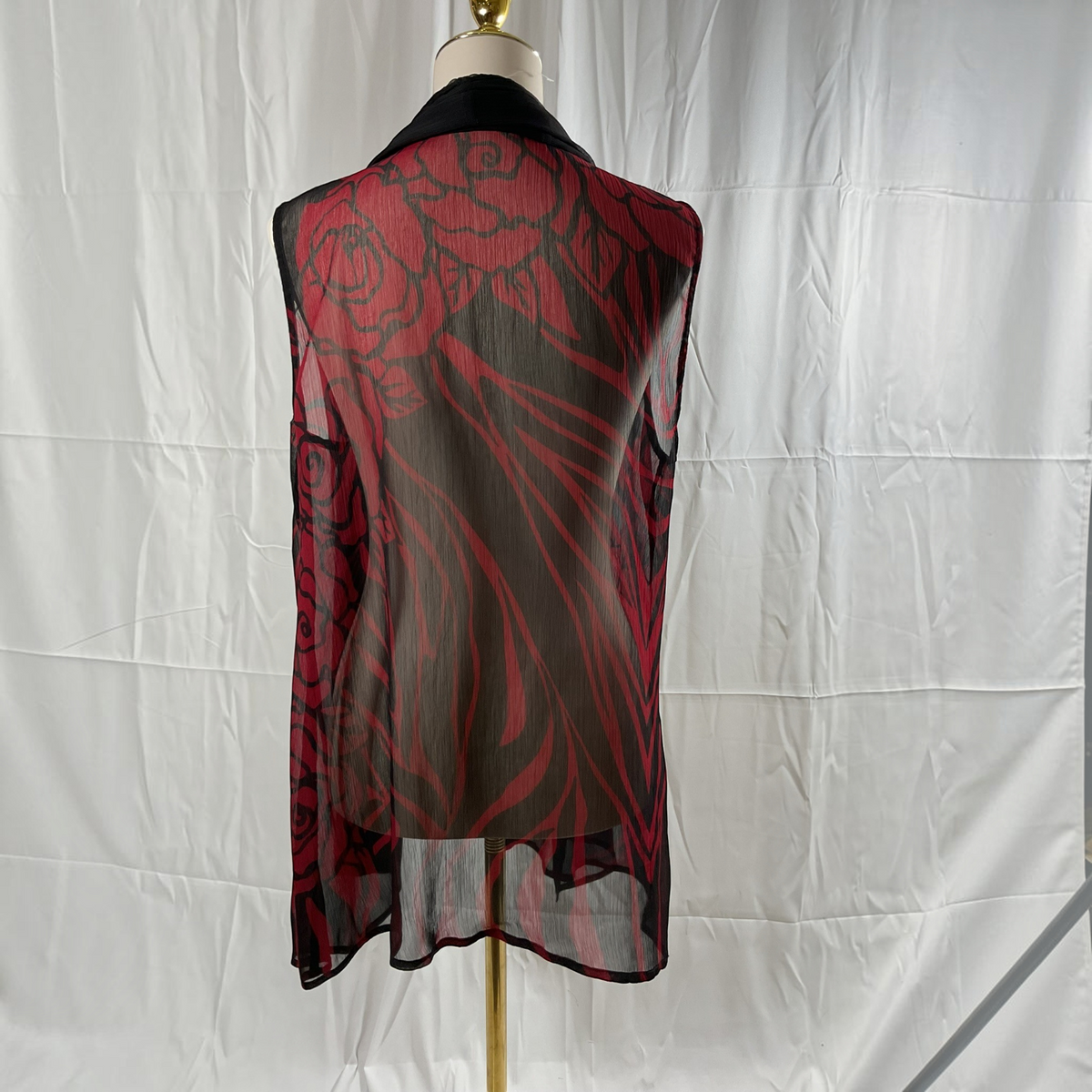 A sheer black mesh vest with a red floral pattern, displayed on a mannequin torso against a white fabric backdrop.