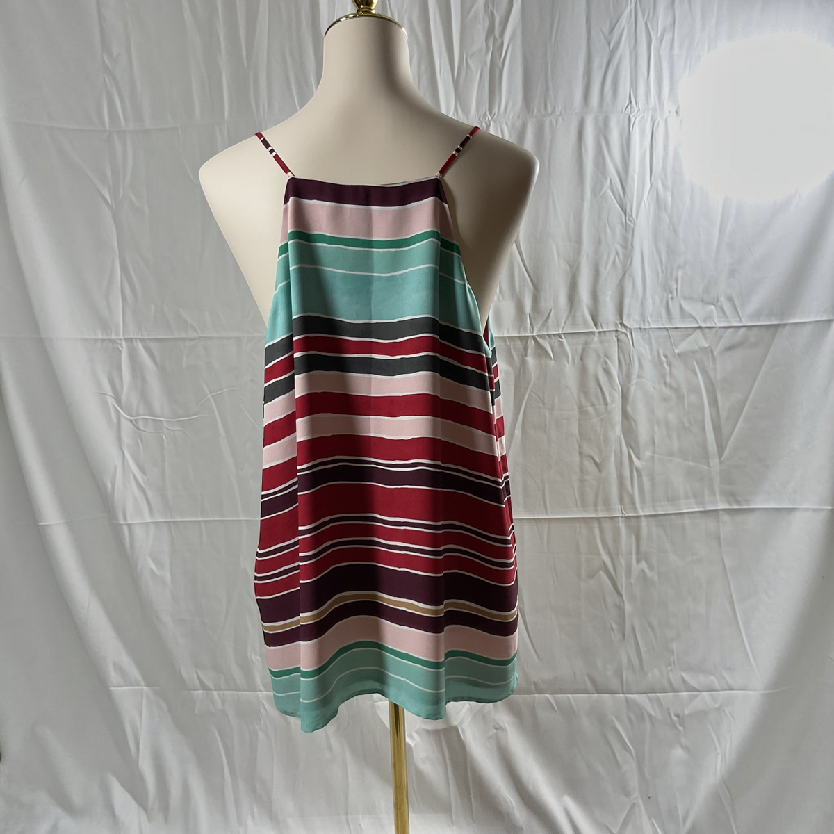 A sleeveless striped camisole dress with thin shoulder straps, displayed on a cream mannequin torso against a wrinkled white fabric backdrop.