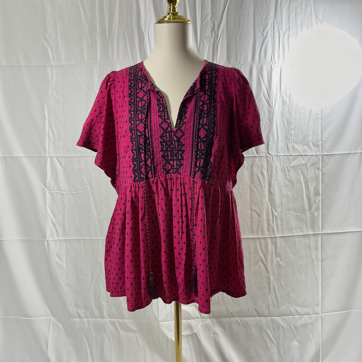 A short-sleeve pink dress with black geometric patterns and polka dots, displayed on a mannequin torso against a white wrinkled backdrop.
