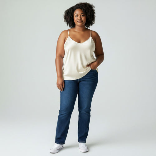 Woman wearing a white tank top and blue jeans on a plain background