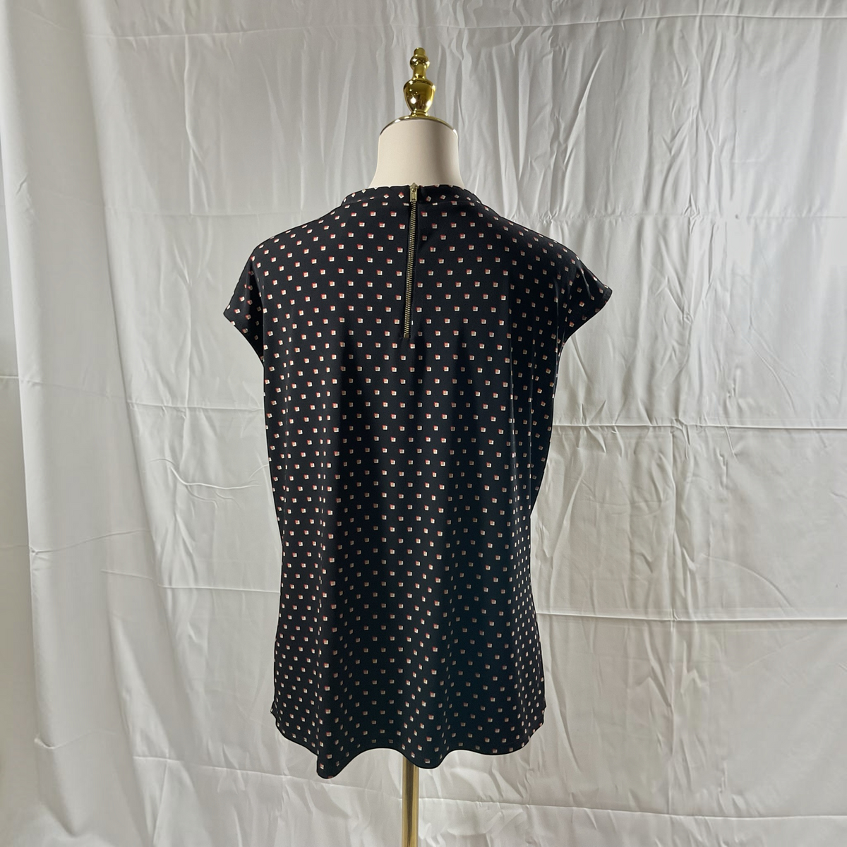 A black short-sleeve top with a white polka dot pattern, displayed on a dress form mannequin against a wrinkled white fabric backdrop.