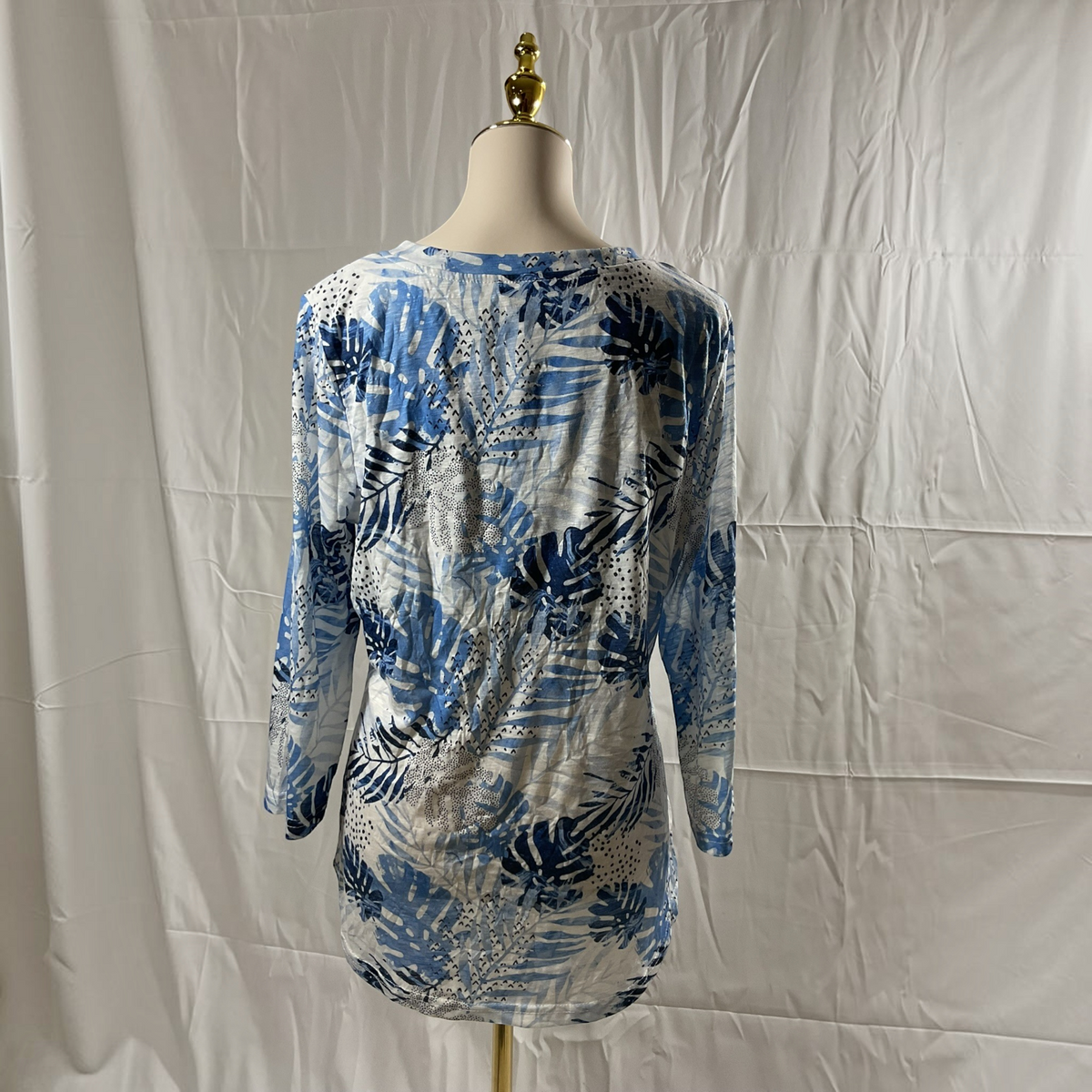 A long-sleeve tunic top with a blue, navy, and white tropical leaf pattern, displayed on a mannequin torso against a white fabric backdrop.
