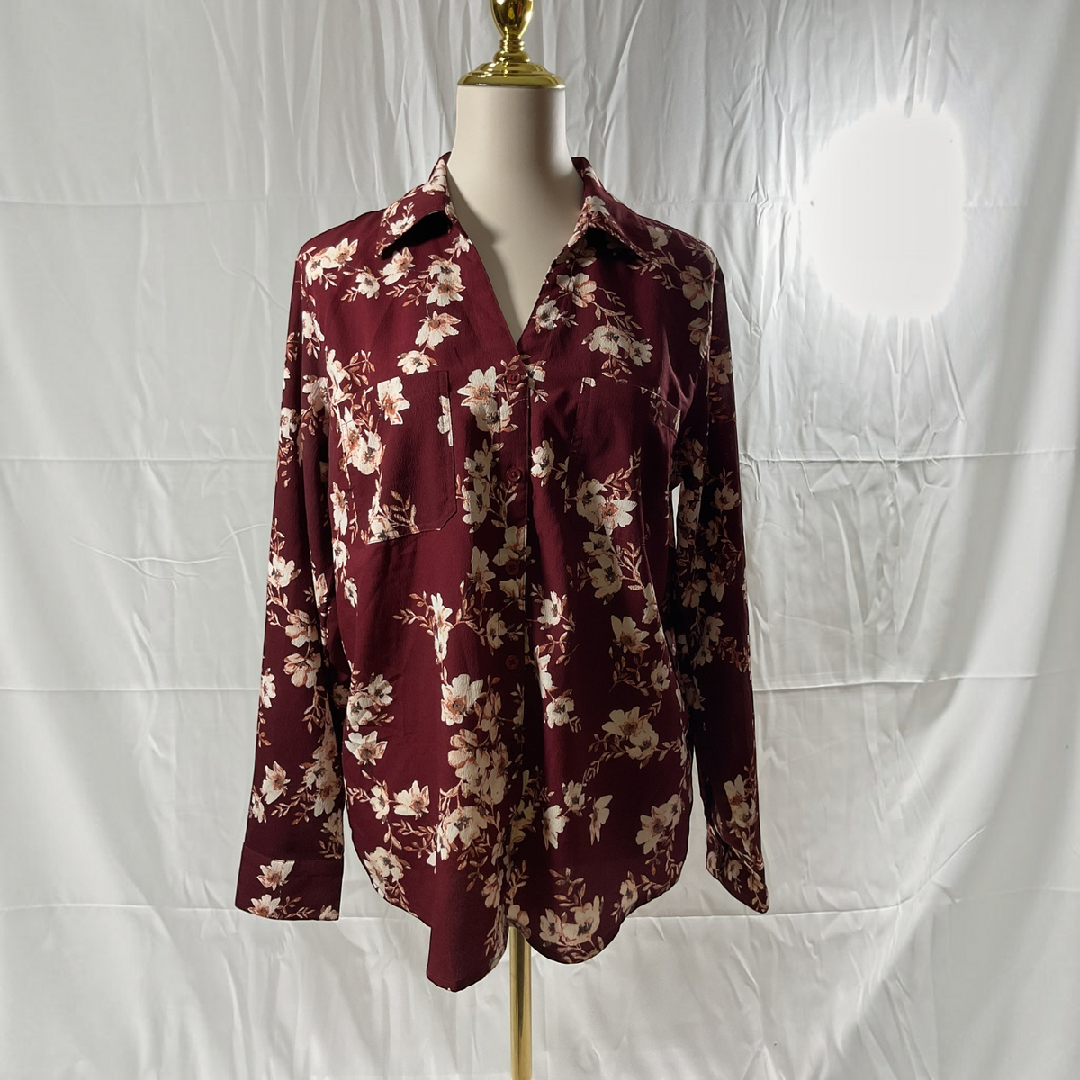 A long-sleeve button-up blouse with a burgundy and beige floral print, displayed on a mannequin torso against a white fabric backdrop.