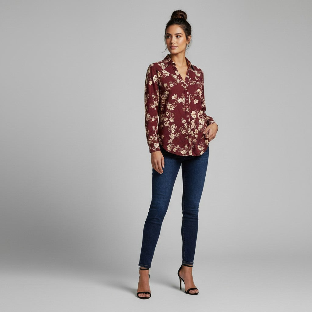A woman modeling a burgundy long-sleeve button-up blouse with a beige floral pattern, paired with dark blue skinny jeans and black high-heeled sandals, against a solid gray studio background.