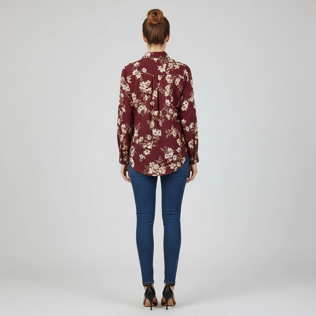 A woman viewed from behind wearing a burgundy long-sleeve button-up shirt with a beige floral pattern, paired with blue skinny jeans and black high heels, against a light gray studio background.