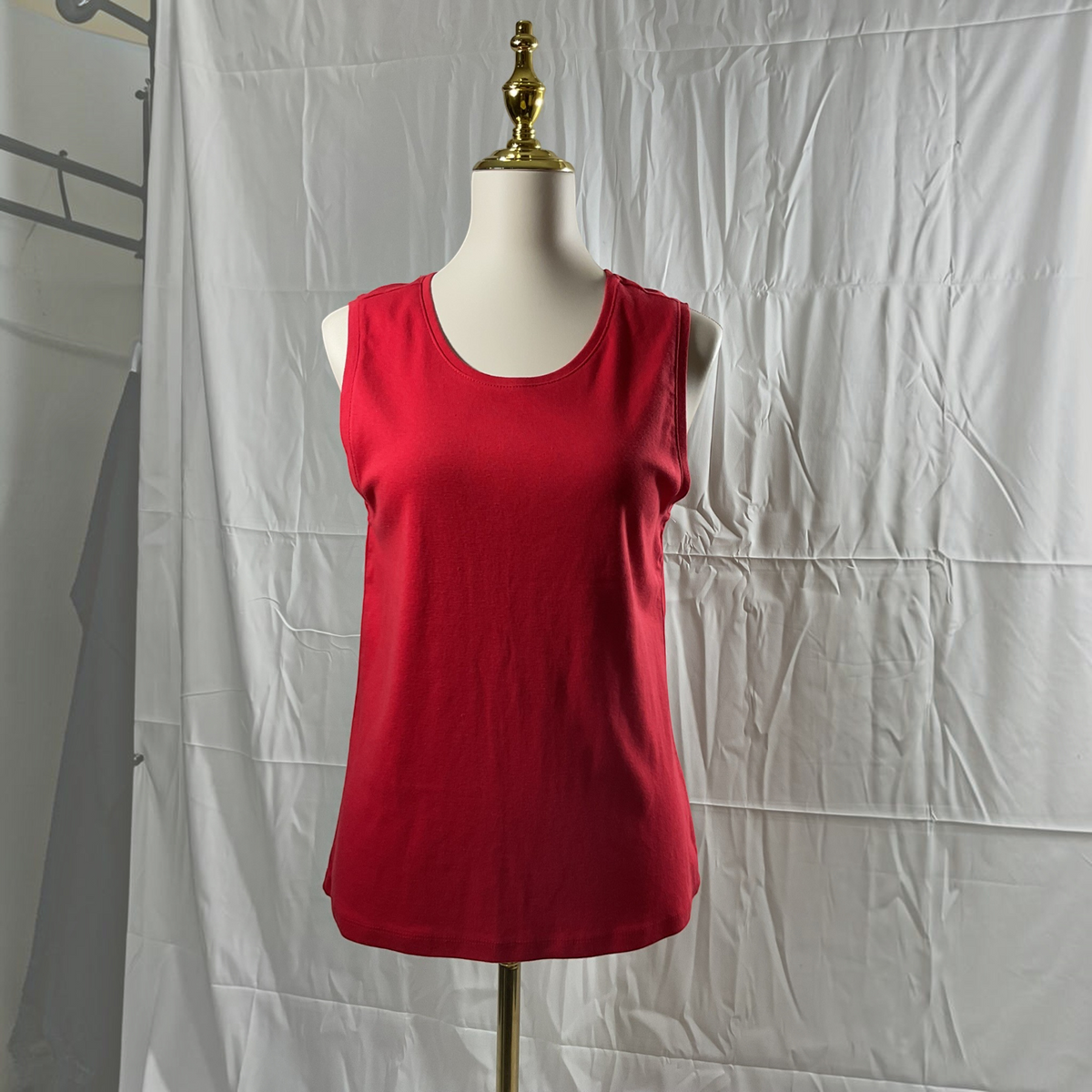 A sleeveless red scoop-neck tank top displayed on a white mannequin torso with a gold neck cap, set against a wrinkled white studio backdrop.