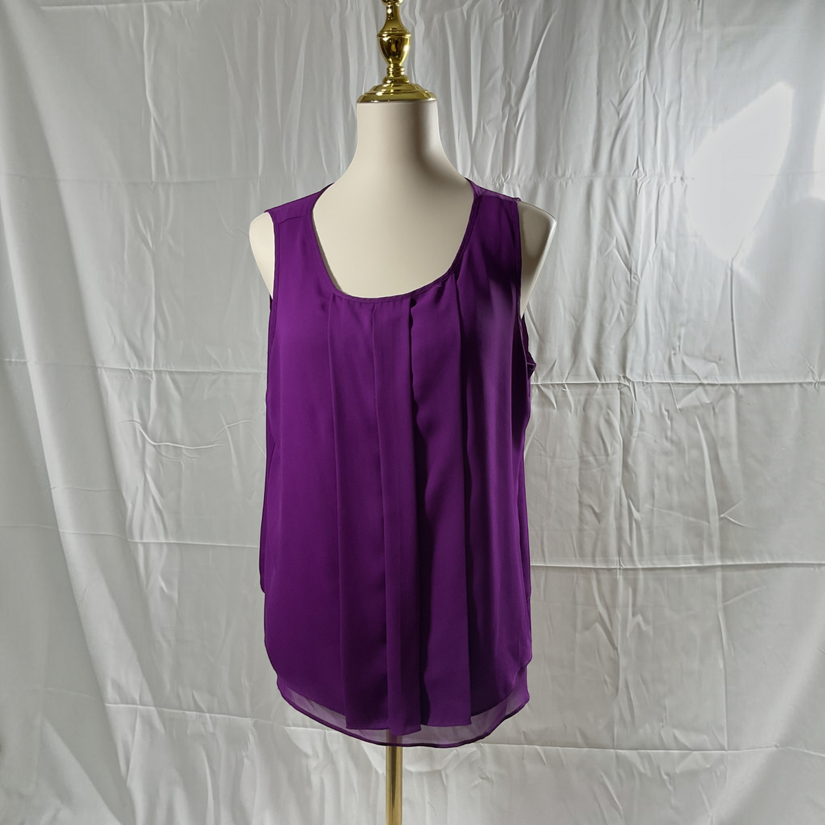 A sleeveless purple blouse displayed on a cream dress form mannequin against a wrinkled white fabric backdrop.