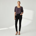 A woman in a dark gray shirt with white dots, black skinny jeans and black high heels on a studio gray background.