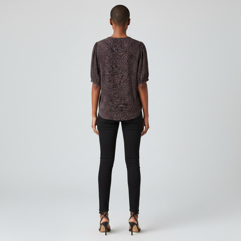 A woman in a dark gray shirt with white dots, black skinny jeans and black high heels on a studio gray background.
